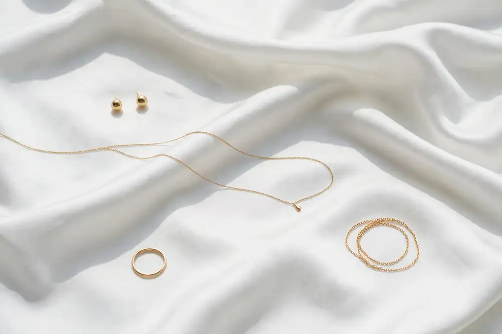 Collection of minimal gold bridal jewelry pieces arranged on white silk