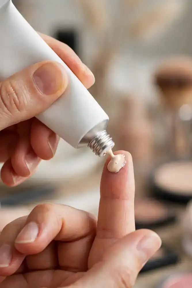 Hands squeezing mattifying primer from a tube onto a fingertip