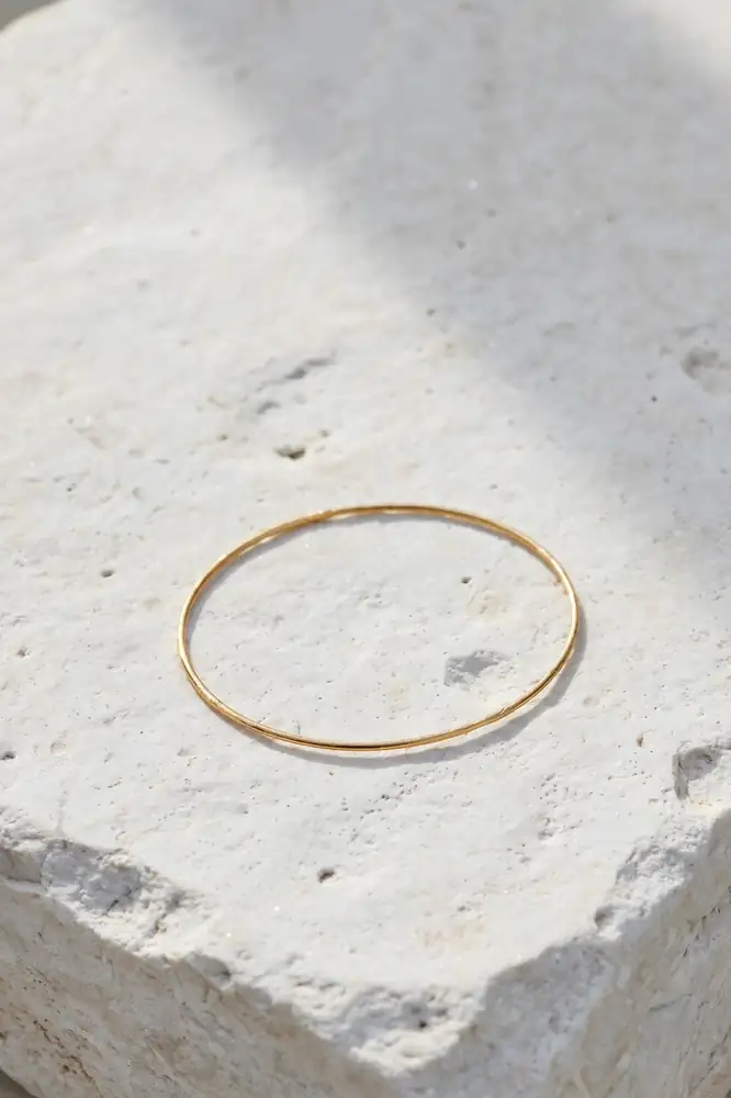 Single thin gold bangle bracelet on a white stone surface