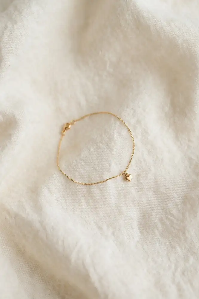 Delicate charm bracelet with one tiny heart charm on cream fabric
