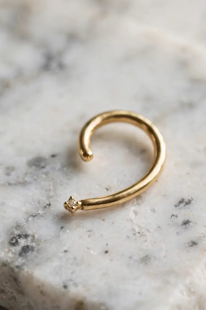 Single gold ear cuff with a tiny stone on a marble surface