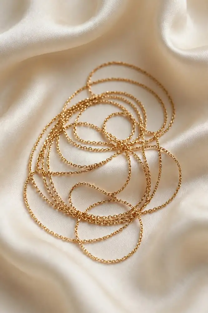 Fine thin gold chain necklace coiled on cream silk fabric