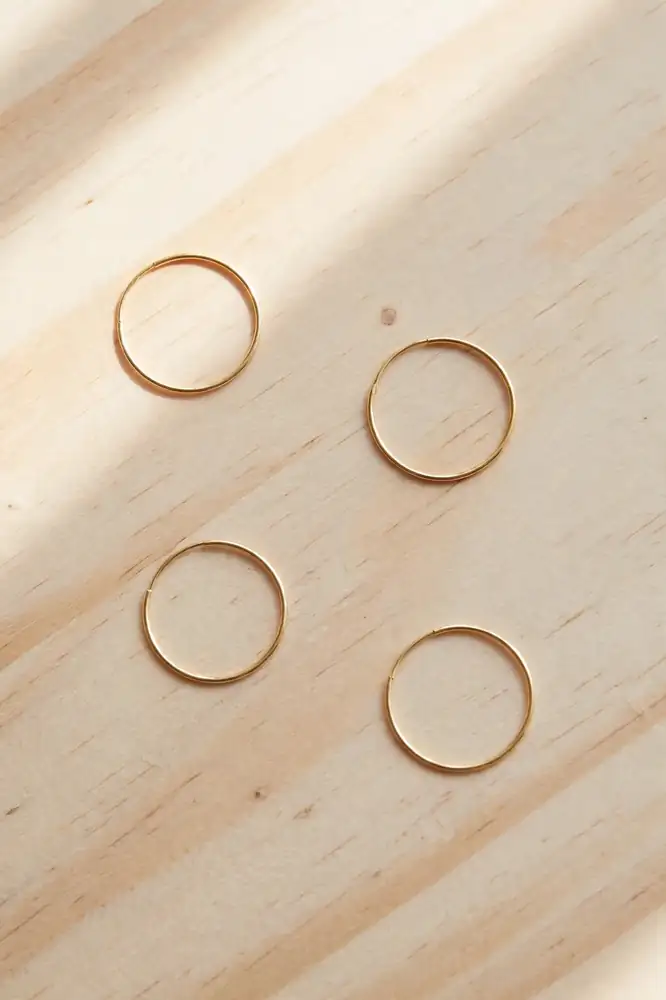 Small thin gold hoop earrings on a light wood surface