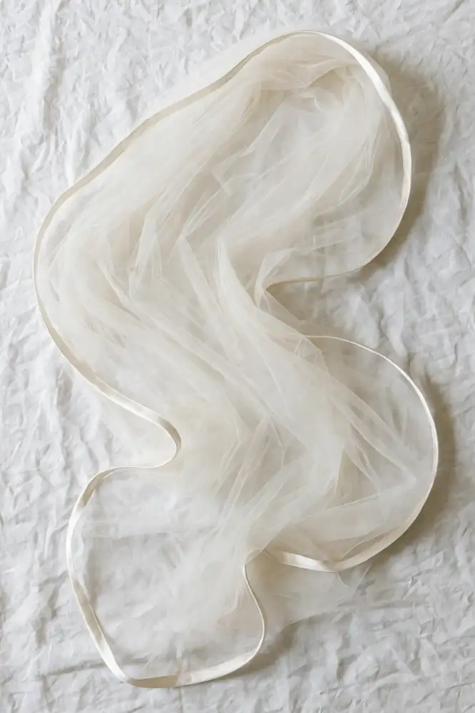 Chapel-length bridal veil with satin edge trim laid flat on white linen