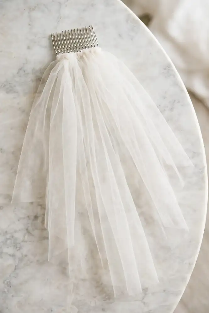 Fingertip-length bridal veil on a metal comb on a marble tabletop